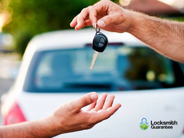Locksmith kneeling at an open car door, working on the lock from inside the frame